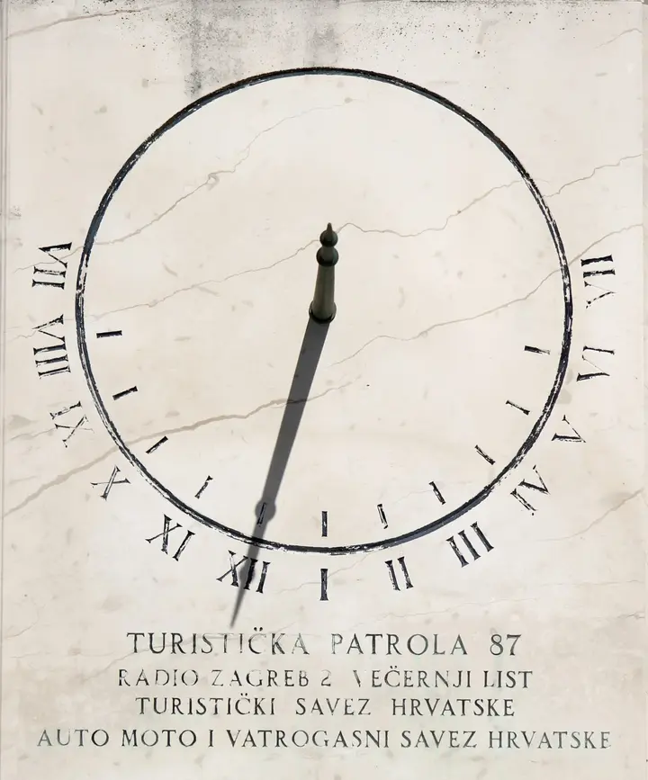 Sundial in Krk, Croatia showing the gnomon (stick) casting a shadow onto the marker at XII 12 o'clock noon. The shadow is shortest at 12 noon and allows people to track the sun.